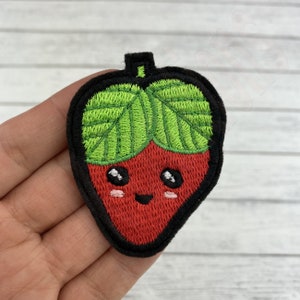 Può includere: Toppa ricamata da stirare a forma di fragola rossa con un cappello verde a foglie e un viso sorridente.