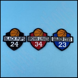 May include: Three embroidered patches with basketballs and team names. The first patch is black with white text that reads "BLACK PUPS" and the number "24". The second patch is red with white text that reads "BROWN LYNXES" and the number "34". The third patch is blue with white text that reads "GOLDEN CUBS" and the number "23".