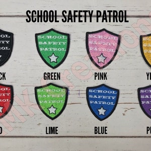 May include: Eight iron-on patches in different colors, each featuring a white shield with the text "SCHOOL SAFETY PATROL" and a white star. The colors are black, green, pink, yellow, red, lime, blue, and purple.