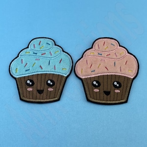 May include: Two embroidered iron-on patches of cupcakes with happy faces. One cupcake is blue with pink sprinkles and the other is pink with yellow sprinkles.