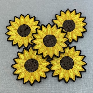 May include: Five yellow embroidered sunflower patches with black centres. The patches are arranged in a cluster on a grey background.