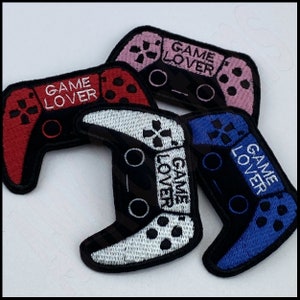 May include: Four embroidered patches in the shape of a video game controller. The patches are in red, pink, white, and blue. Each patch has the text "GAME LOVER" on it.
