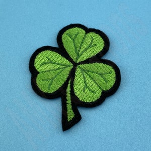 May include: A green shamrock patch with black stitching. The shamrock is a traditional Irish symbol of good luck.