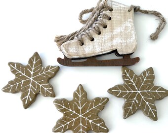 Puede incluir: Adorno de patín de hielo de madera con acabado blanco envejecido y base marrón, junto con tres adornos de copo de nieve marrón con detalles blancos. Ideal para la decoración de invierno o festiva.