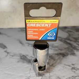May include: A chrome universal joint socket with a black and orange label. The label reads "CRESCENT" and "UNIVERSAL JOINT" in English, French, and Spanish. The socket is designed for use with a 1/2-inch drive.