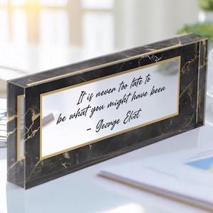 May include: A black and gold desk plaque with a marble pattern and the quote "It is never too late to be what you might have been - George Eliot".
