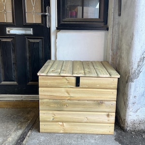 May include: A wooden storage box with a hinged lid and a black metal latch. The box is made of natural wood and has a light brown colour.