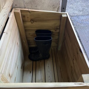 May include: A wooden storage box with a hinged lid, open to reveal two pairs of black rubber boots inside.