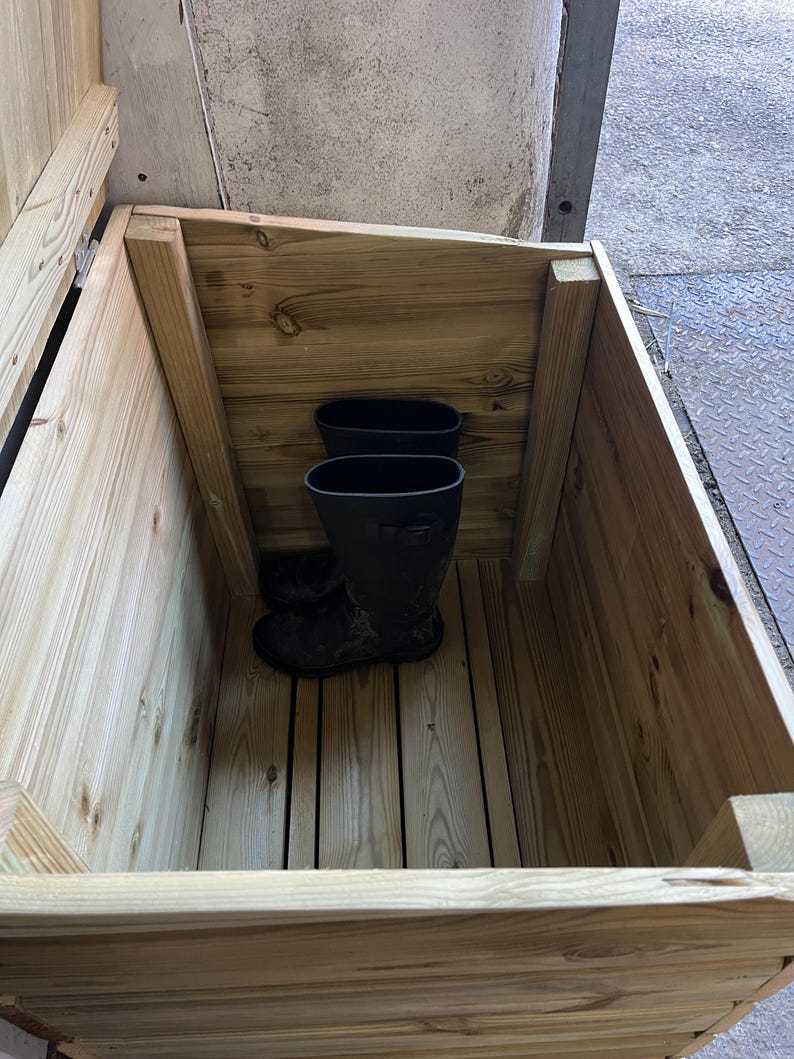 May include: A wooden storage box with a hinged lid, open to reveal two pairs of black rubber boots inside.