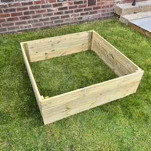 May include: A square wooden raised garden bed, made from natural wood planks. The bed is sitting on a green lawn.