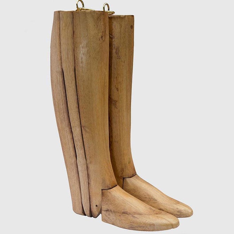 May include: A pair of wooden boot trees with a light brown finish. The boot trees are made of multiple pieces of wood that are joined together. The boot trees have a hook at the top for hanging.