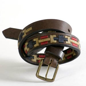 Könnte beinhalten: Ein brauner Ledergürtel mit einem gewebten Muster in Rot, Blau und Gold. Der Gürtel hat eine silberne Schnalle.