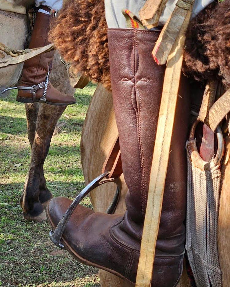May include: Close-up of brown leather riding boots with spurs and stirrups. The boots are worn by a rider on horseback. The image highlights the equestrian equipment and the texture of the leather.