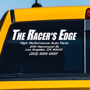 May include: A yellow pickup truck with a white decal on the back window that reads "THE RACER'S EDGE", "High Performance Auto Parts", "2710 Hammond St.", "Los Angeles, CA 90033", and "(213) 555-0157".