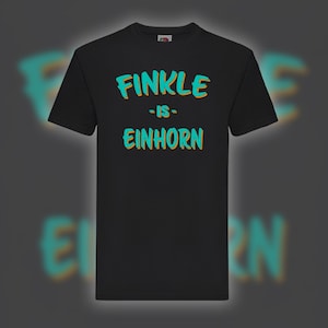 May include: Black t-shirt with the text "FINKLE - IS - EINHORN" in turquoise and orange lettering. The shirt is a classic crew neck style, suitable for casual wear. The design is centered on the front of the shirt.