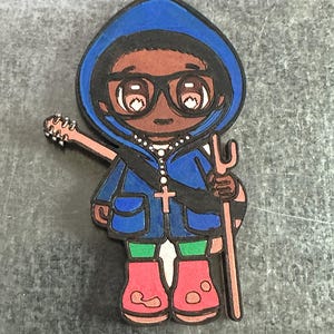 Könnte beinhalten: Eine Comicfigur, die eine blaue Kapuzenjacke, eine Brille und rote Stiefel trägt. Die Figur hält einen Stock und eine Gitarre. Die Figur trägt eine Halskette mit einem Kreuz.