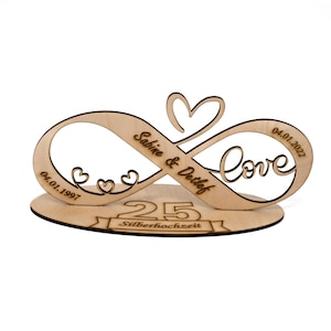 Könnte beinhalten: Holz-Unendlichkeitszeichen mit dem Text "Sabine & Detlef" und "Love" eingraviert. Die Daten "04.01.1997" und "04.01.2022" sind ebenfalls in das Symbol eingraviert. Die Zahl "25" und der Text "Silberhochzeit" sind auf einem Band unter dem Symbol eingraviert.