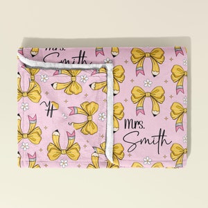 May include: Pink fleece blanket with a yellow bow and pencil pattern. The blanket has the text "mrs. Smith" on it.