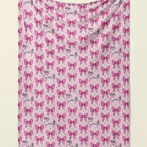 May include: Pink throw blanket with a repeating pattern of pink bows and the text "Mrs. Smith" in a cursive font.