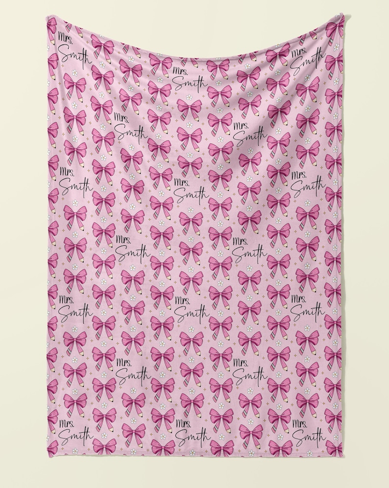 May include: Pink throw blanket with a repeating pattern of pink bows and the text "Mrs. Smith" in a cursive font.