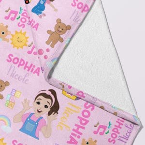 May include: Pink baby blanket with a repeating pattern of cartoon characters, musical notes, and the name "Sophia Nicole" in pink. The blanket features a white, soft, plush backing.