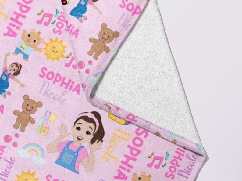 May include: Pink baby blanket with a repeating pattern of cartoon characters, musical notes, and the name "Sophia Nicole" in pink. The blanket features a white, soft, plush backing.