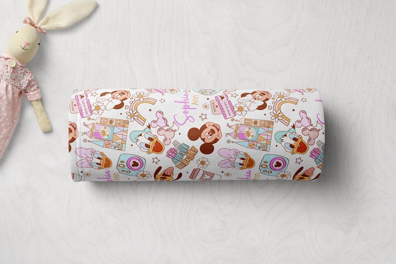 Puede incluir: Tela blanca con un patr&oacute;n repetido de Mickey Mouse, Minnie Mouse y Donald Duck. Los personajes est&aacute;n en un estilo de dibujos animados y est&aacute;n rodeados de detalles coloridos como arco&iacute;ris, estrellas y corazones. La tela tambi&eacute;n presenta el texto "Sophia Ann".