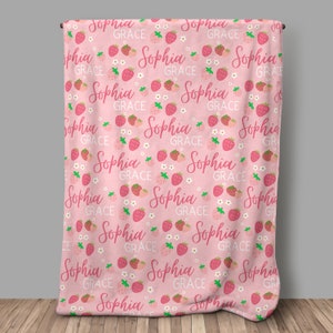 Pode incluir: Cobertor rosa para beb&ecirc; com um padr&atilde;o repetido de morangos, flores brancas e o nome "Sophia Grace" em escrita rosa.