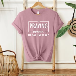 Puede incluir: Una camiseta rosa con el texto "Praying mama all day. everyday." en letras blancas.