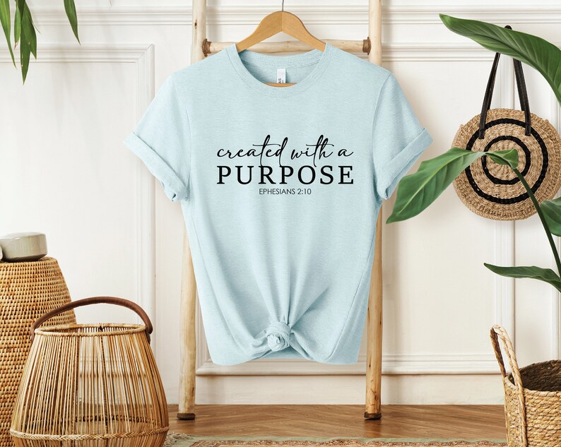 Puede incluir: Camiseta azul claro con el texto "created with a PURPOSE" y "EPHESIANS 2:10" en letras negras.
