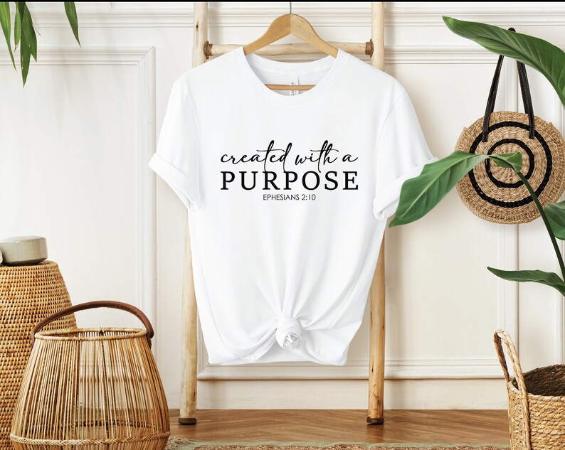 Puede incluir: Camiseta blanca con el texto "created with a PURPOSE" y "EPHESIANS 2:10" impreso en negro.