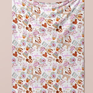 Puede incluir: Una manta de beb&eacute; blanca con un patr&oacute;n repetido de Mickey Mouse, Minnie Mouse, Donald Duck y Goofy. El patr&oacute;n tambi&eacute;n incluye corazones, estrellas, arco&iacute;ris y el texto "Sophia Ann".