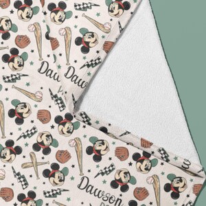 May include: A white towel with a Mickey Mouse baseball theme. The towel features a repeating pattern of Mickey Mouse wearing a baseball cap and holding a bat, along with baseballs, bats, and lightning bolts. The text "Daw Daw" is printed on the towel.