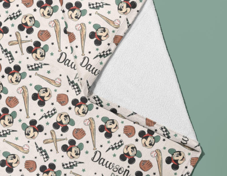 May include: A white towel with a Mickey Mouse baseball theme. The towel features a repeating pattern of Mickey Mouse wearing a baseball cap and holding a bat, along with baseballs, bats, and lightning bolts. The text "Daw Daw" is printed on the towel.