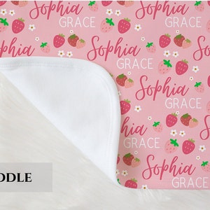 Pode incluir: Cobertor de embrulho rosa com forro de minky branco. O cobertor apresenta um padr&atilde;o repetido de morangos e o nome "Sophia Grace" em uma fonte de letra rosa.