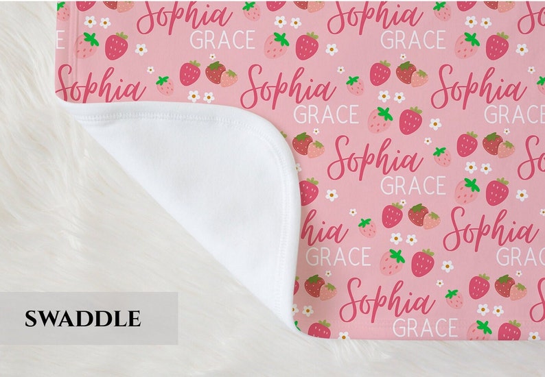 Pode incluir: Cobertor de embrulho rosa com forro de minky branco. O cobertor apresenta um padr&atilde;o repetido de morangos e o nome "Sophia Grace" em uma fonte de letra rosa.