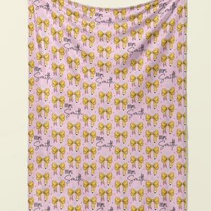 May include: Pink fleece blanket with a repeating pattern of yellow bows and the text "Mrs. Smith" in black script.