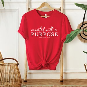 Puede incluir: Camiseta roja con texto blanco que dice "created with a PURPOSE" y "EPHESIANS 2:10".