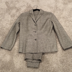 May include: A gray tweed suit jacket and matching pants. The jacket has a single-breasted closure with four buttons and a notched lapel.