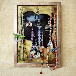 May include: A framed display with a silhouette of a face, showcasing a variety of jewelry including necklaces, bracelets, and earrings. The jewelry features a mix of colors, including green, blue, red, and purple, with intricate designs and beads.