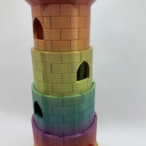 May include: A multi-colored tower-shaped dice rolling tray with a rainbow gradient. The tower has four levels with a rounded base and a small opening on the side. The top level has a crenellated design.