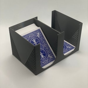 May include: A gray, three-compartment card holder with a geometric design on the sides. The holder contains two decks of blue playing cards. The cards have a white and blue design on the back.