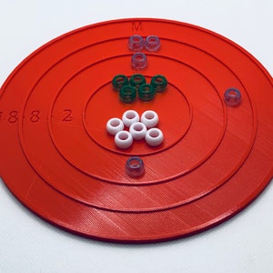 May include: An orange circular board with concentric rings and the numbers 1, 8, 8, and 2 printed on the outer ring. The board has white, green, and purple beads arranged in a pattern on the board. The letter "M" is printed on the top of the board.