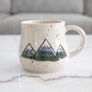 May include: A set of three ceramic mugs with a speckled, matte finish. The mugs are in shades of cream, light gray, and dark gray. Each mug has a simple, minimalist design, perfect for coffee or tea.