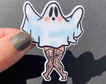 May include: A sticker of a cartoon ghost with a pale blue sheet, rosy cheeks, and black eyes. The ghost has legs in black fishnet stockings with spiderweb patterns. The sticker is set against a black backdrop.