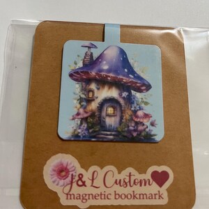 May include: A brown card with a blue and white mushroom house illustration and the text "J&L Custom magnetic bookmark" in pink and white.