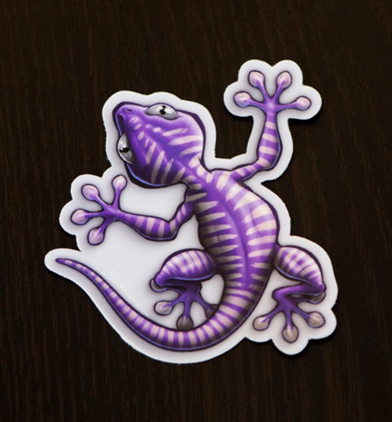 K&ouml;nnte beinhalten: Ein Aufkleber mit einem lila und wei&szlig;en Gecko mit einem gestreiften Muster. Der Gecko befindet sich in einer Kletterpose mit eingerolltem Schwanz.