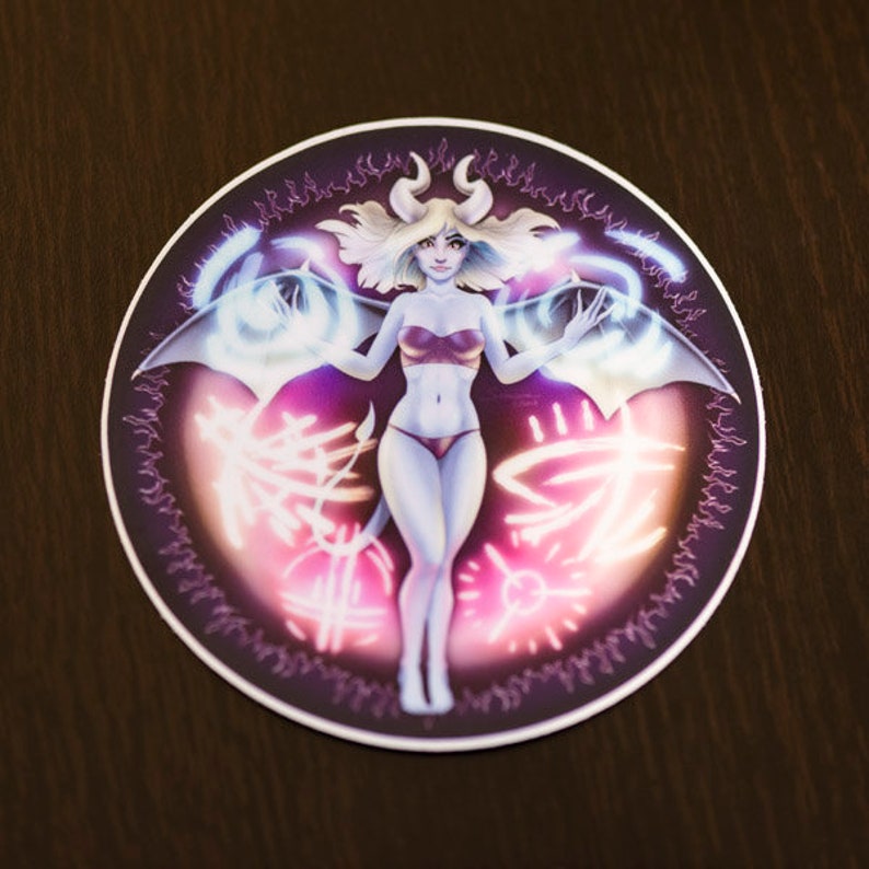 May include: A round sticker featuring a digital illustration of a woman with horns and wings. She is wearing a red bikini top and a purple skirt. The background is a dark purple with glowing pink and white accents.