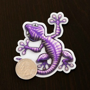 K&ouml;nnte beinhalten: Lilafarbener und wei&szlig;er Gecko-Aufkleber mit einem gestreiften Muster. Der Gecko befindet sich in einer Kletterpose mit eingerolltem Schwanz.