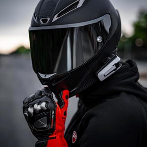 Könnte beinhalten: Schwarzer Motorradhelm mit getöntem Visier. Der Helm hat ein Karbonfasermuster und silberne Akzente. Das Bild zeigt auch schwarze und rote Motorradhandschuhe.